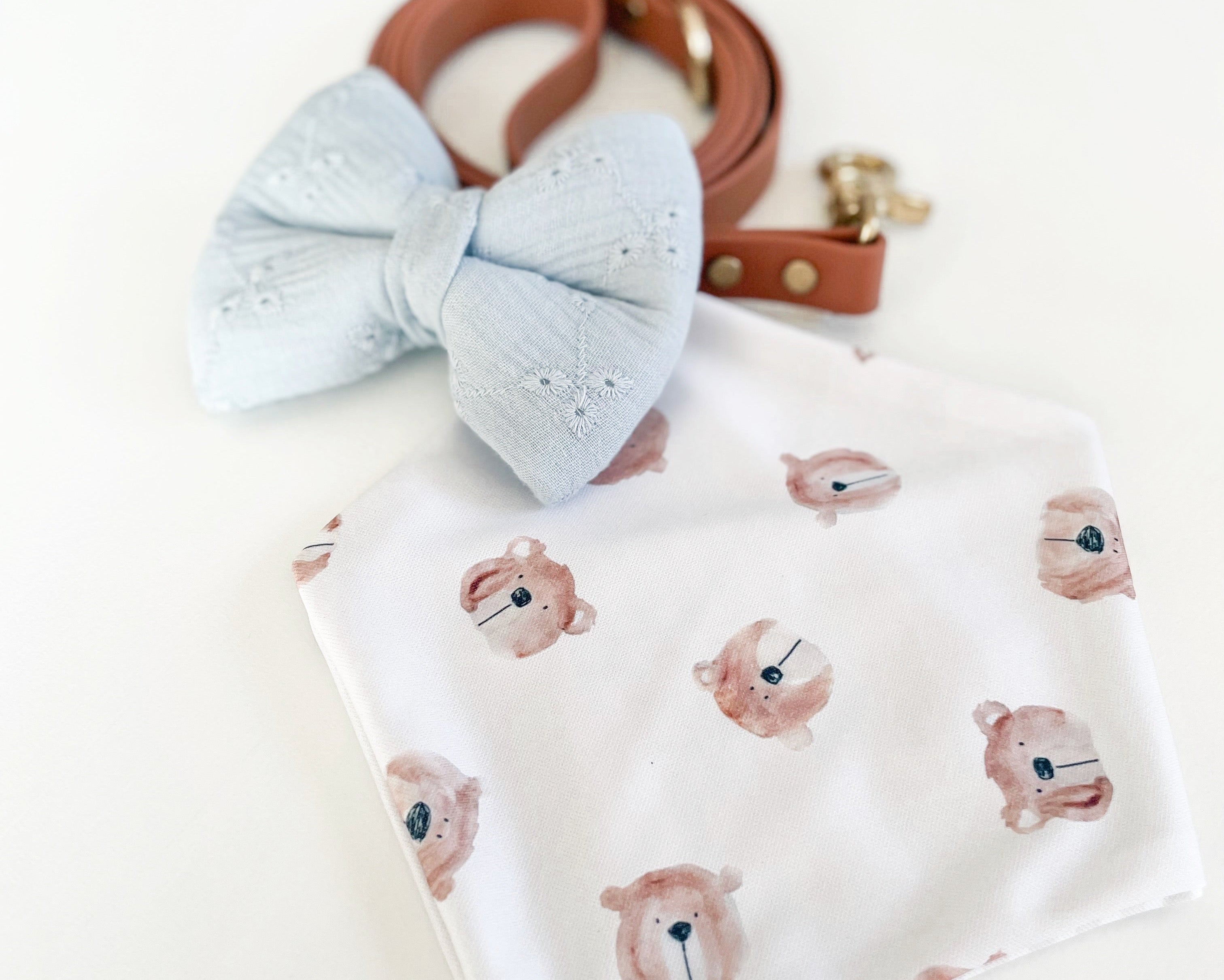 Baby bib with bear pattern, blue bow, and brown leather strap on a white background
