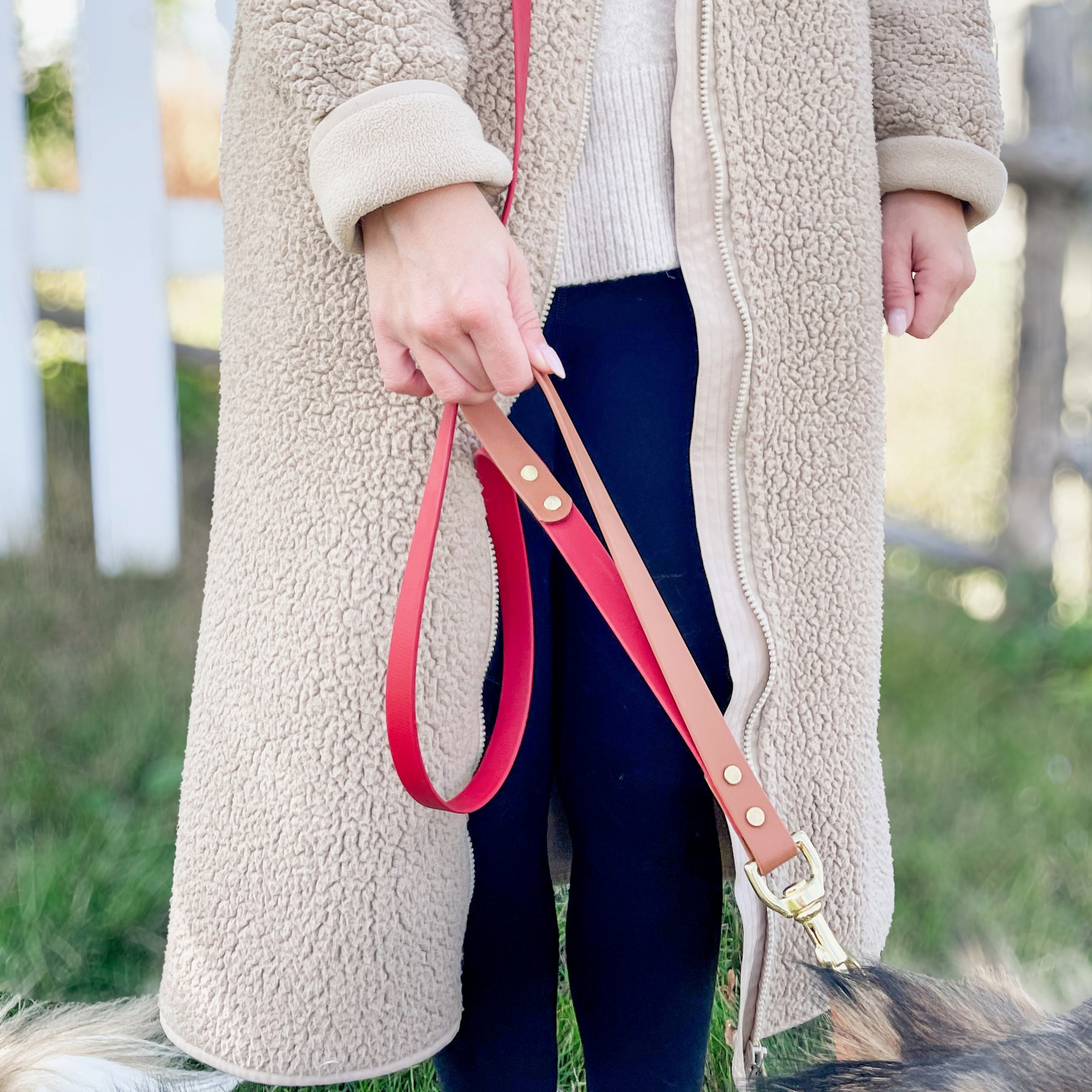 Person holding a red leash with a dog in a grassy area